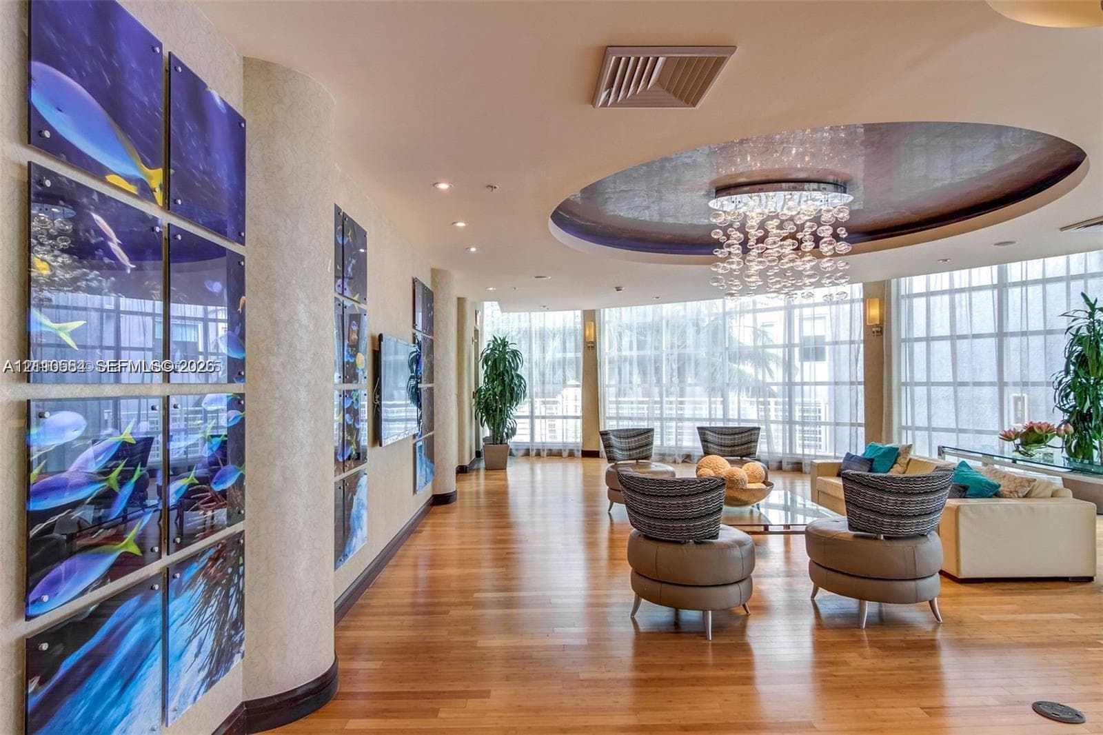 Living area featuring wood-finish flooring, floor-to-ceiling windows, circular recessed ceiling detail, and a multi-tiered crystal chandelier