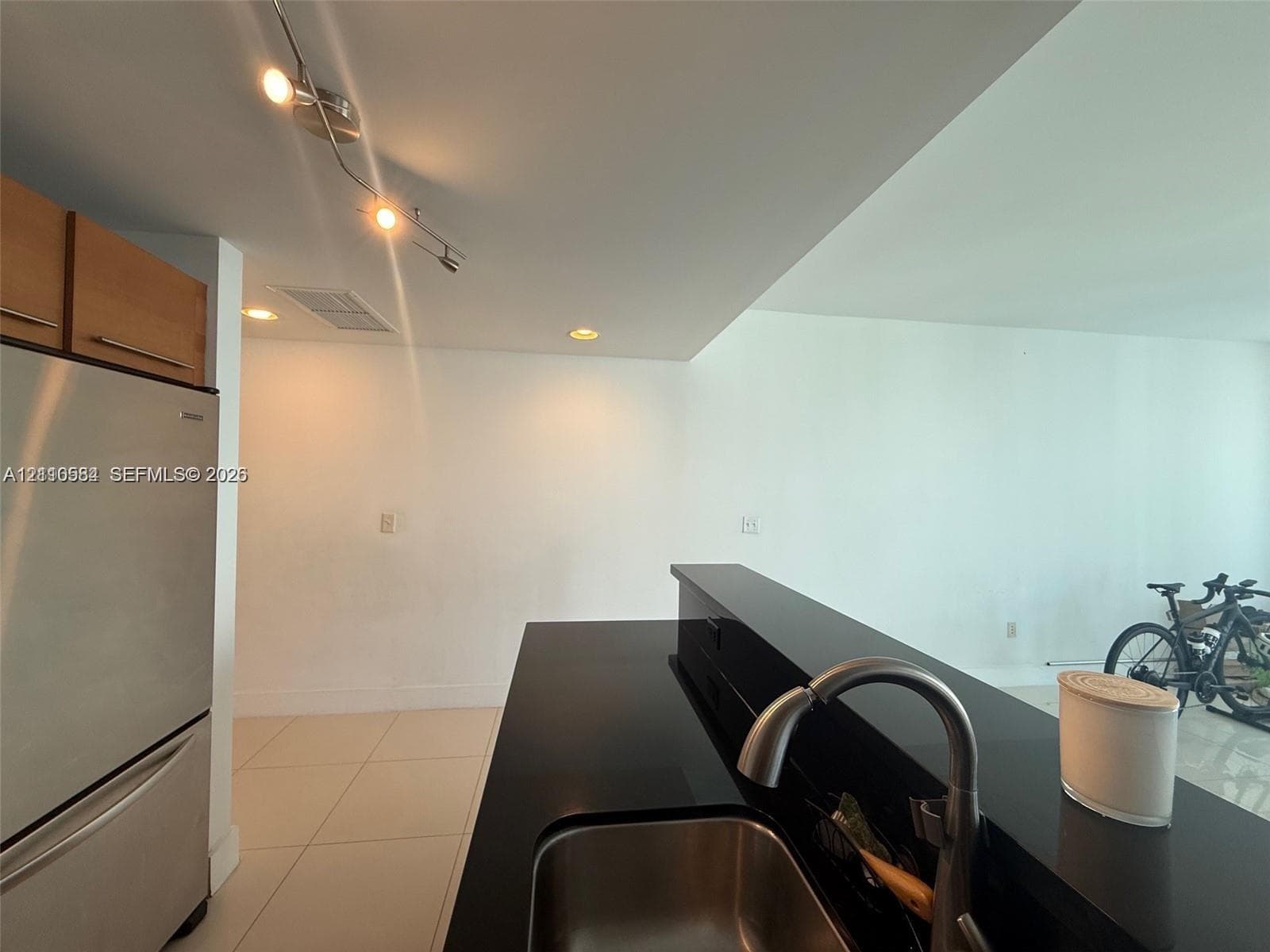 Kitchen featuring a black stone countertop, stainless steel undermount sink, brushed nickel faucet, stainless steel refrigerator, and track lighting