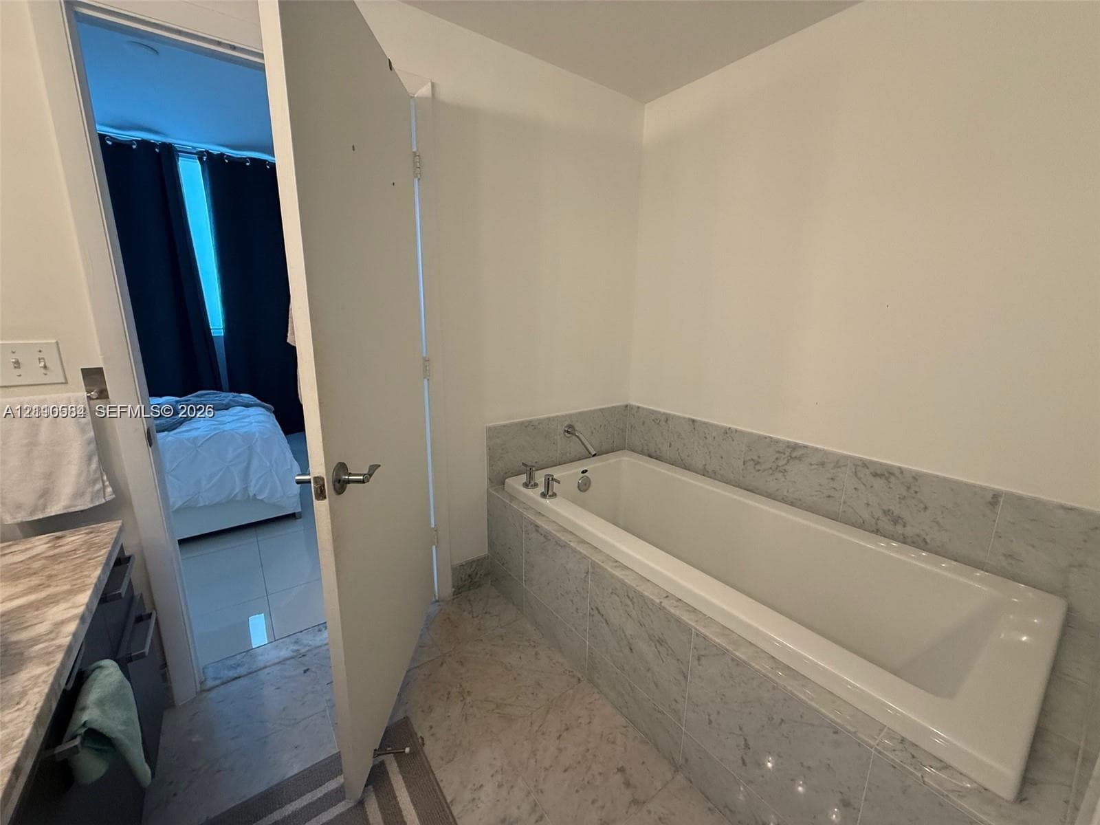 Built-in soaking tub featuring light-toned stone-finish tile surround and integrated plumbing fixtures