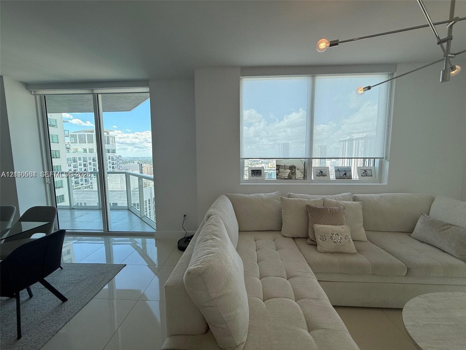 Large-format tile flooring, floor-to-ceiling glass sliding doors, private balcony, solar shades, and architectural multi-arm ceiling lighting