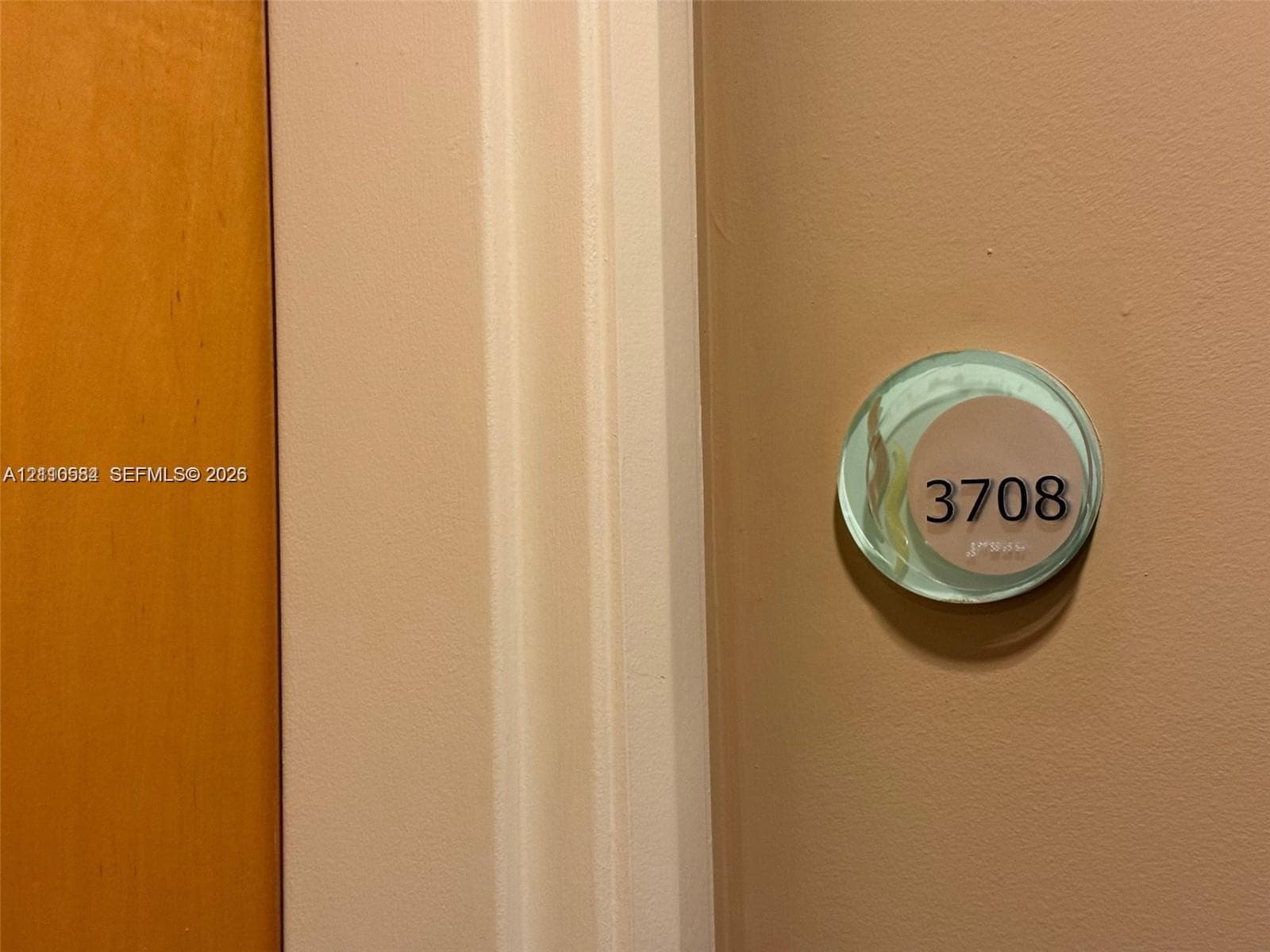 Circular unit identification plaque featuring clear acrylic casing and bold numerical typography mounted on a textured beige wall