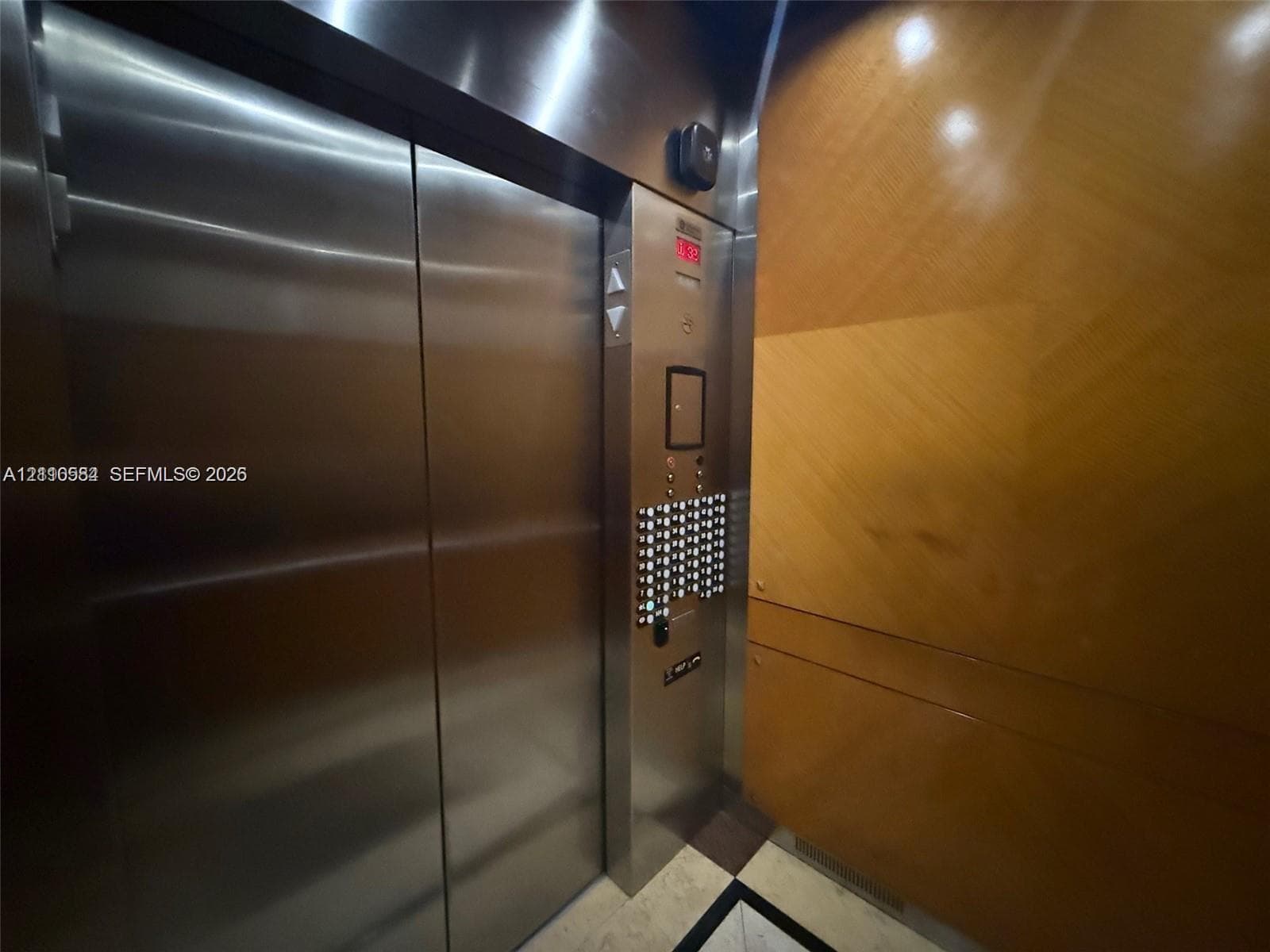 Elevator featuring stainless steel doors, brushed metal control panel, and wood-paneled wall finish