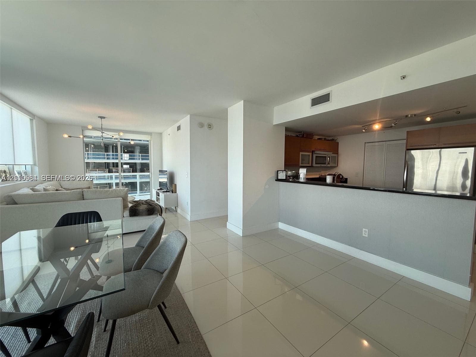 Open-concept interior featuring large-format tile flooring, a kitchen breakfast bar, wood-finish cabinetry, and floor-to-ceiling windows