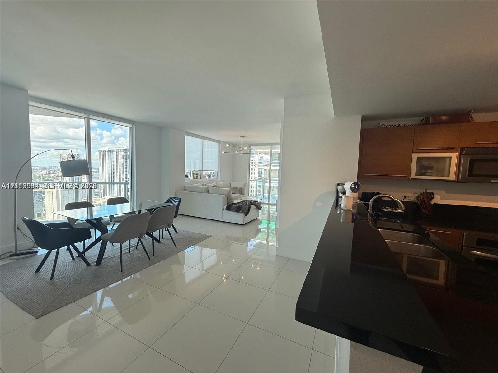 Open-concept living space featuring high-gloss tile flooring, floor-to-ceiling windows, a black countertop breakfast bar, and flat-panel wood cabinetry