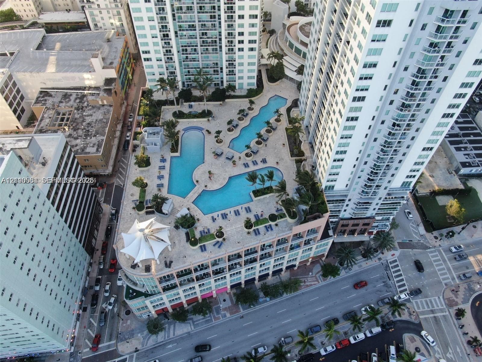 Multi-level swimming pool complex featuring paved decking, lush landscaping, and integrated canopy structures
