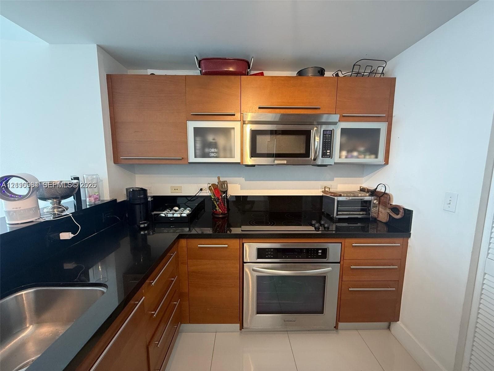 Kitchen featuring wood-finish cabinetry with frosted glass inserts, black stone countertops, stainless steel appliances, and large-format floor tiling