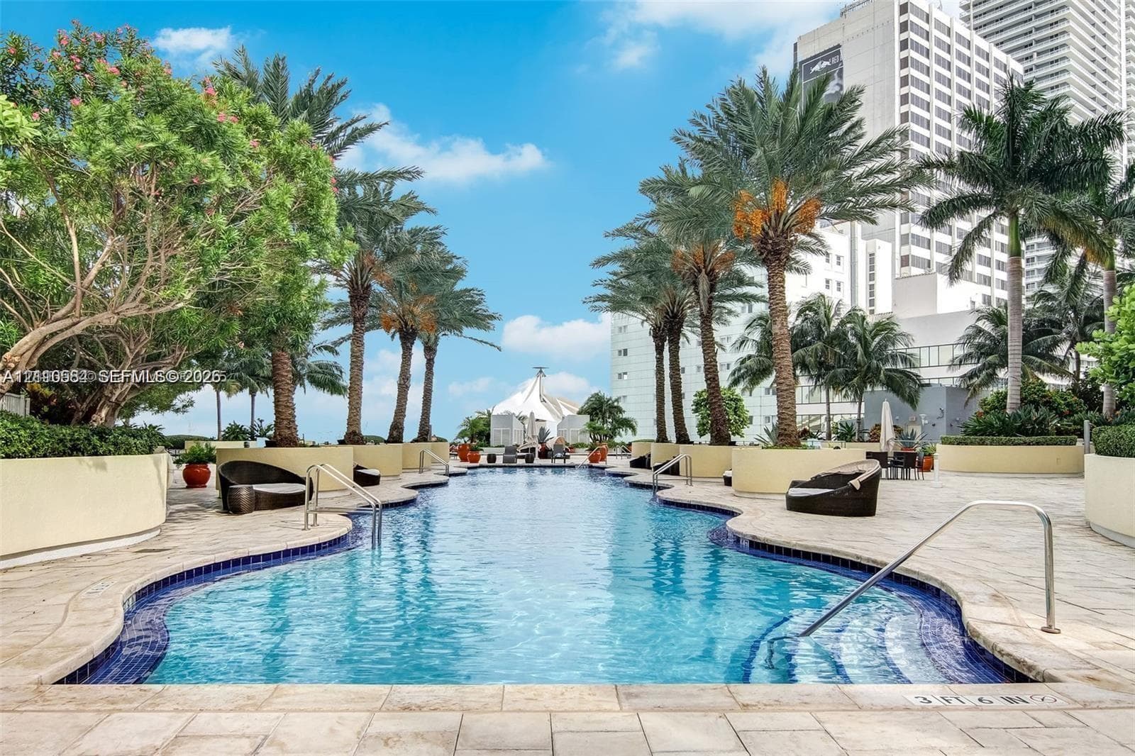 In-ground pool featuring blue tiled accents, stepped entry, stone-tiled pool deck, mature palm trees, and integrated concrete planters