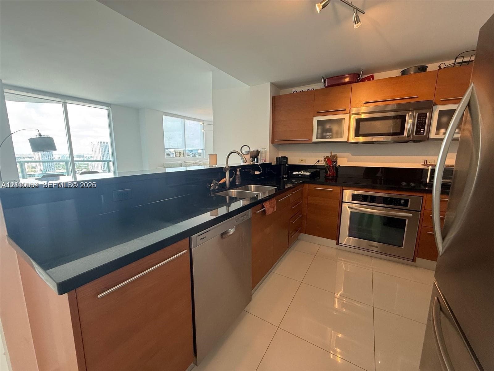 Kitchen featuring wood-veneer cabinetry, dark countertops, stainless steel appliances, and large-format tile flooring