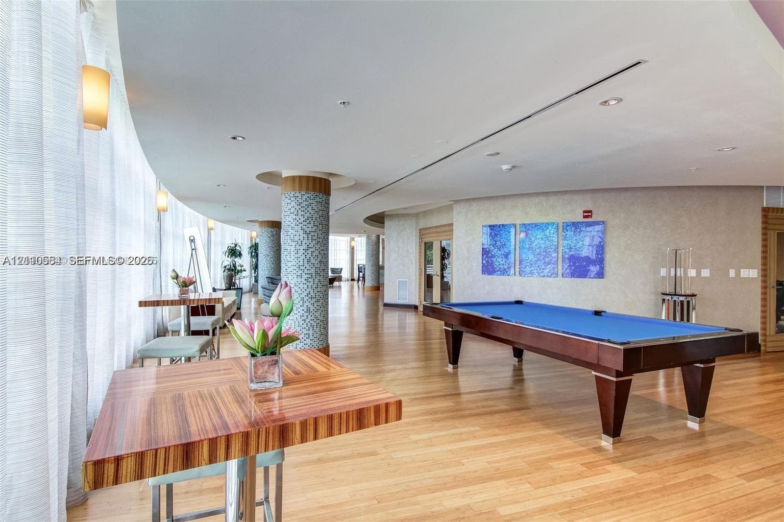 Curved floor-to-ceiling windows, wood-finish flooring, mosaic-tiled structural columns, and recessed ceiling lighting