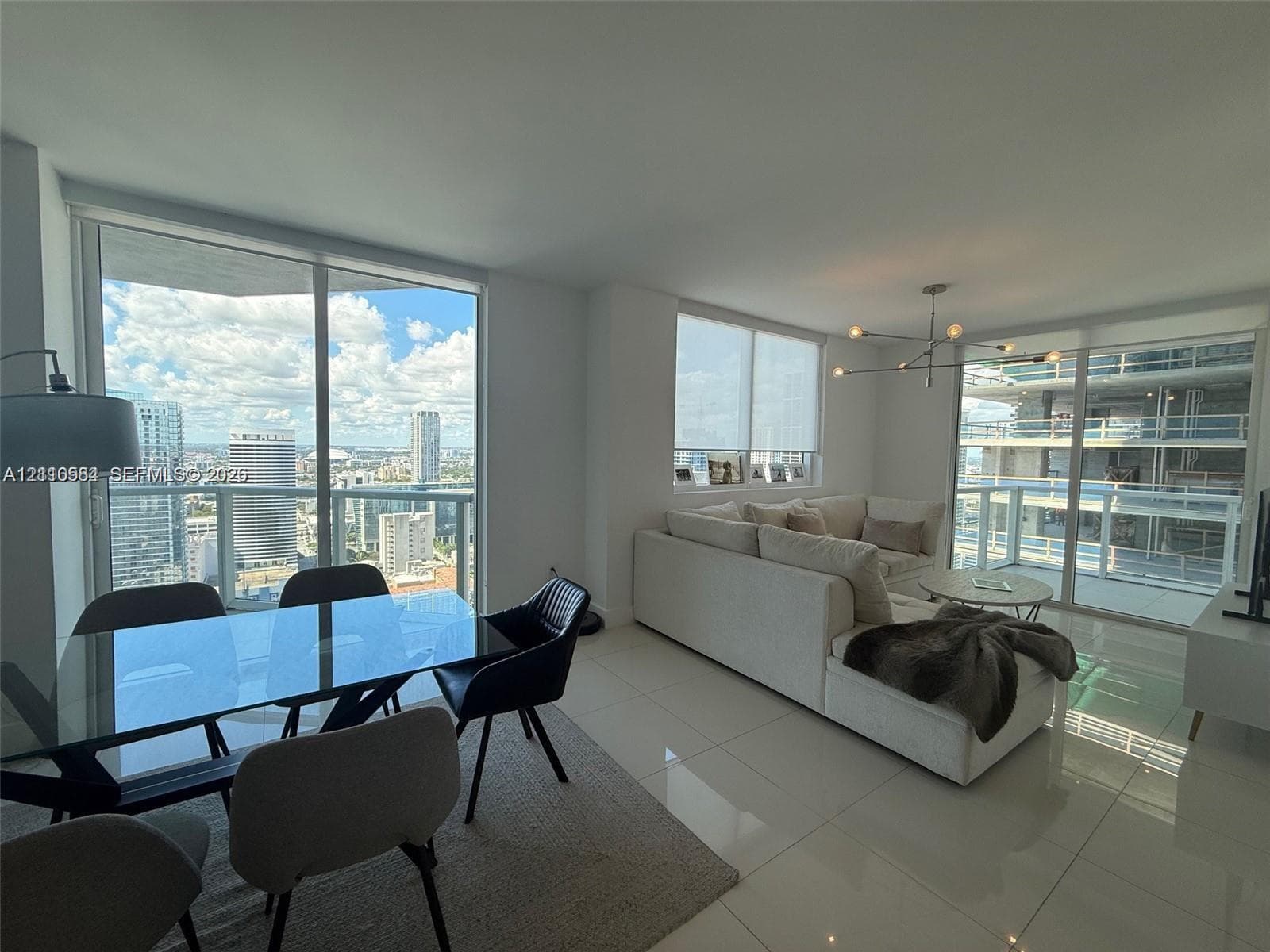 Open-concept living space featuring floor-to-ceiling glass windows, high-gloss tile flooring, sliding glass doors, and a modern multi-arm chandelier