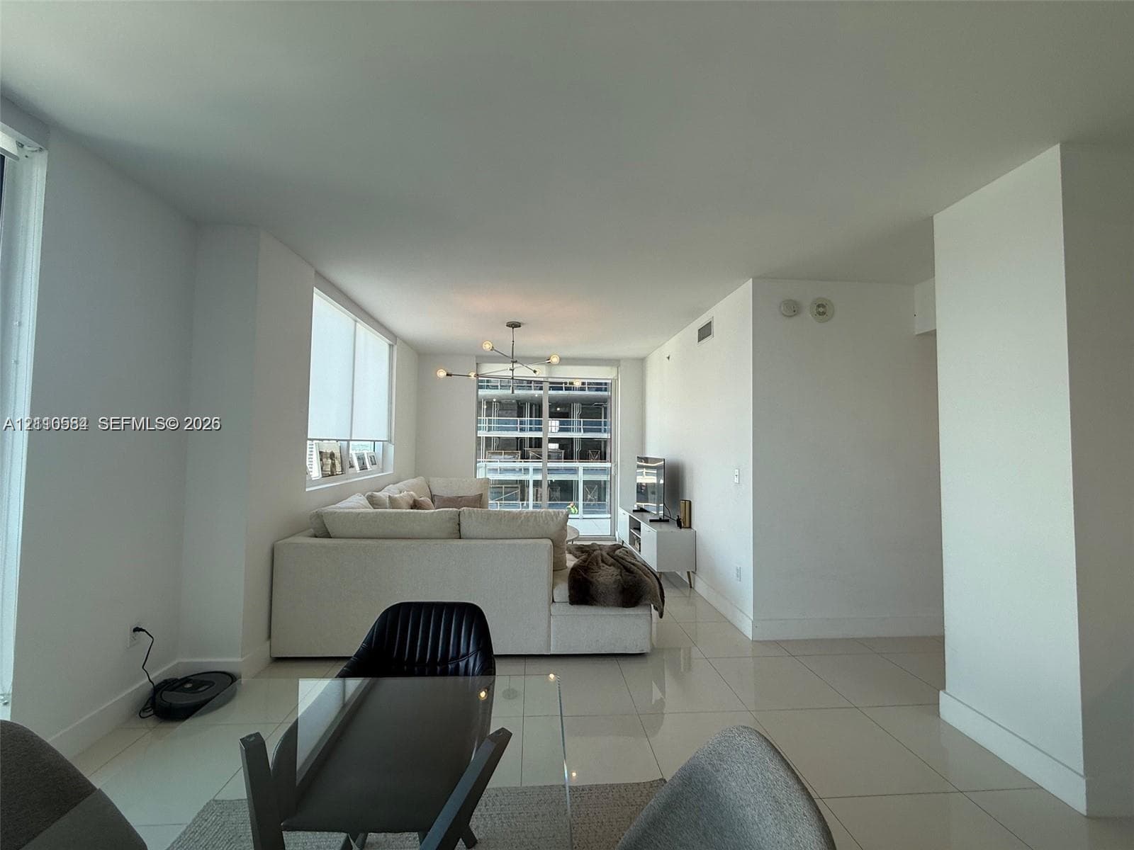 Open-concept interior featuring large-format tile flooring, floor-to-ceiling windows, roller shades, and a multi-arm modern pendant light fixture
