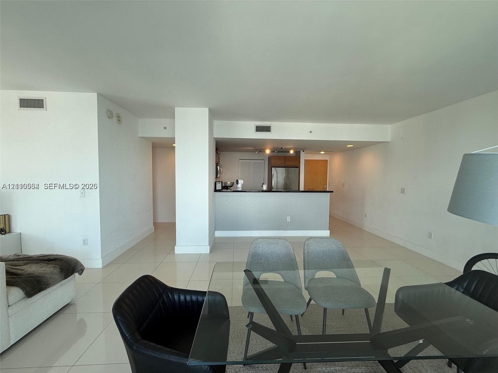Open-concept interior featuring oversized light-toned tile flooring, recessed ceiling lighting, and a kitchen peninsula with a dark countertop