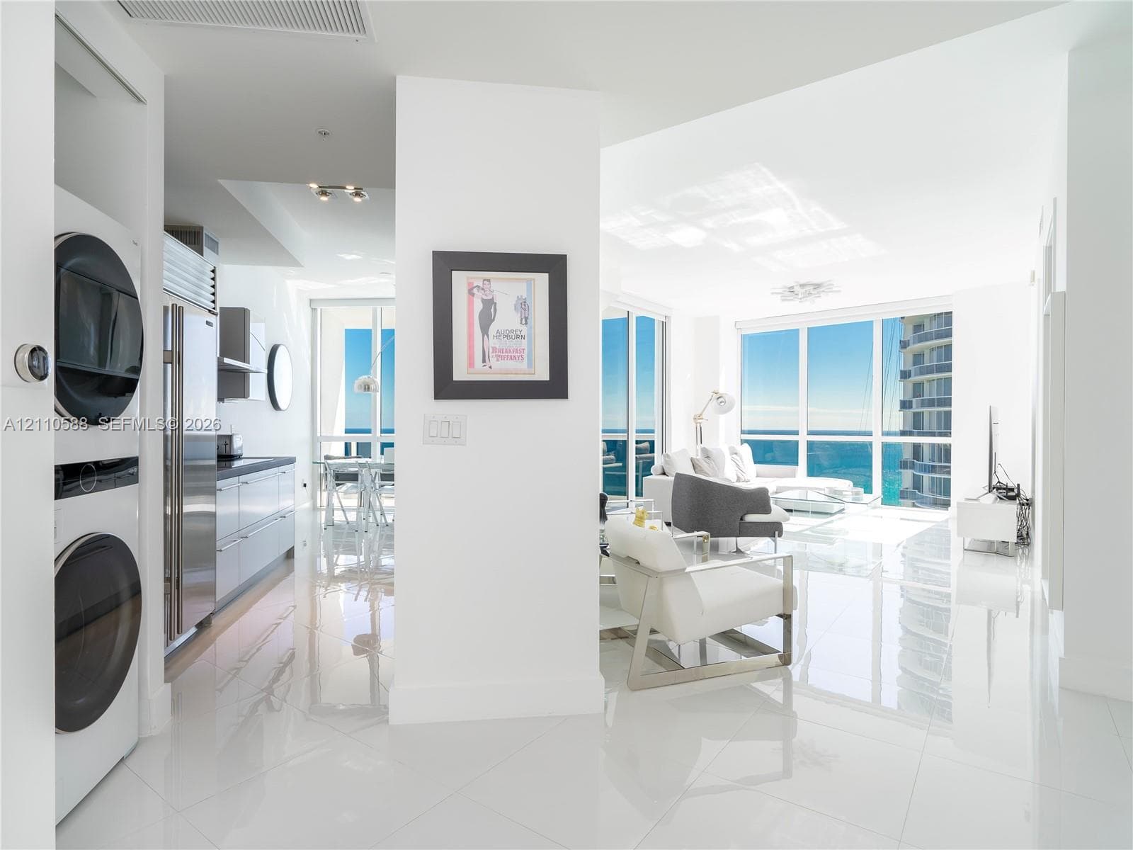 Polished tile flooring, floor-to-ceiling windows, built-in stacked laundry unit, and stainless steel kitchen appliances