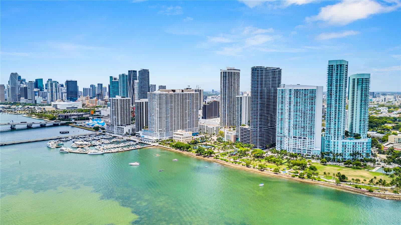Aerial perspective of a coastal cityscape featuring high-rise architecture, an established marina with boat slips, and waterfront park space