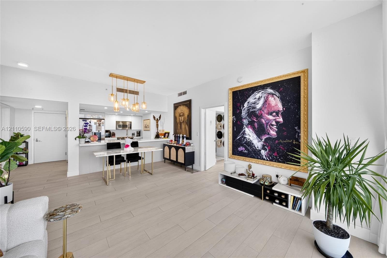 Open-concept interior featuring light-toned wood-finish flooring, recessed lighting, and a multi-pendant brass light fixture