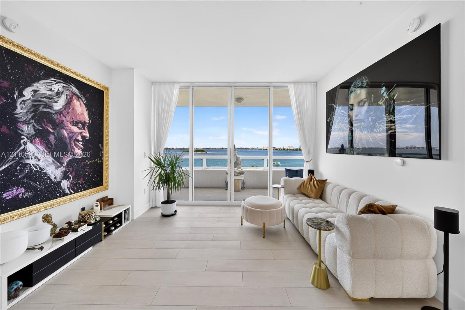 Floor-to-ceiling sliding glass doors, neutral tile flooring, and a private covered balcony featuring water frontage