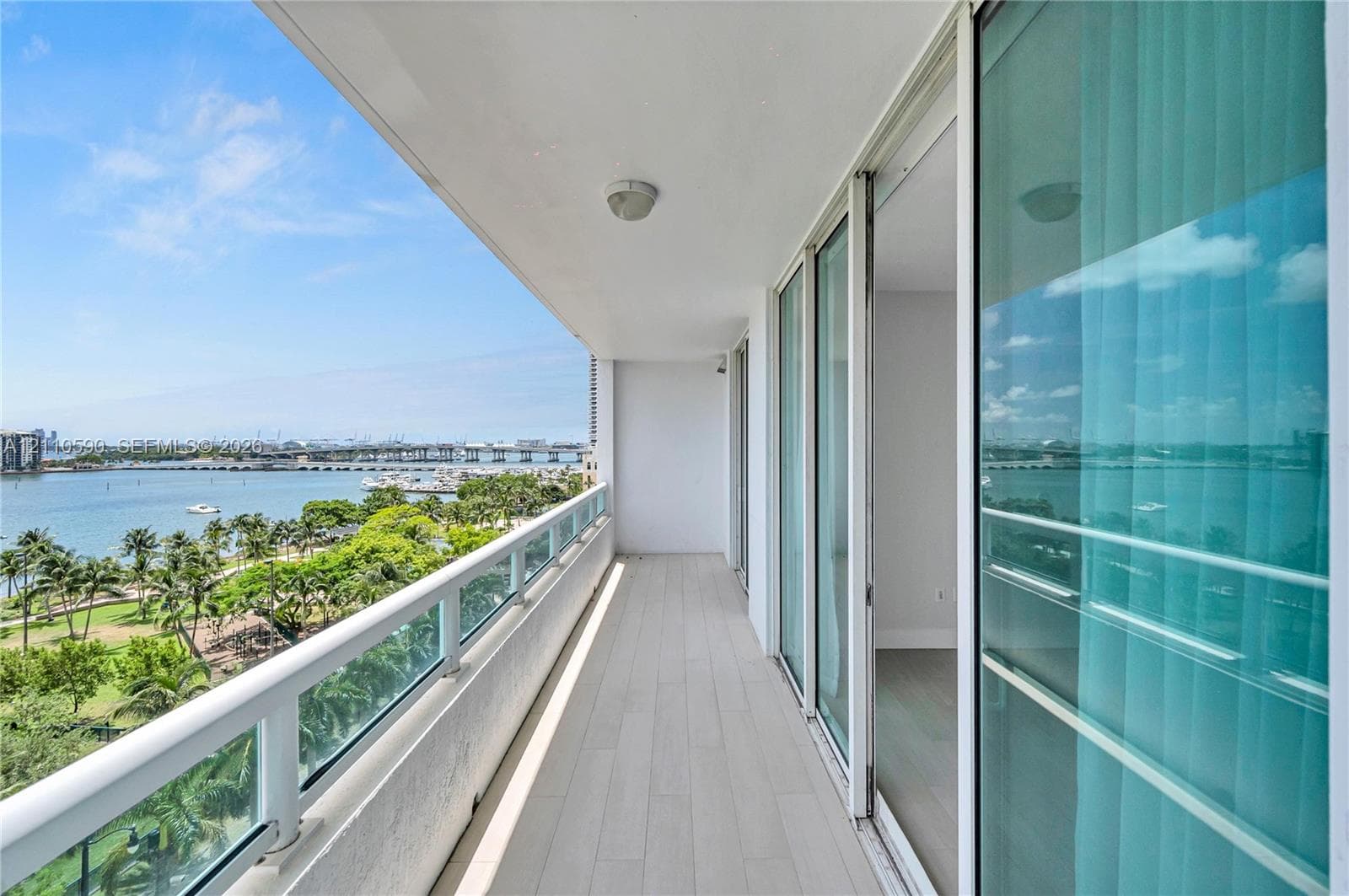 Covered balcony featuring wood-finish tile flooring, glass-panel railings, and floor-to-ceiling sliding glass doors