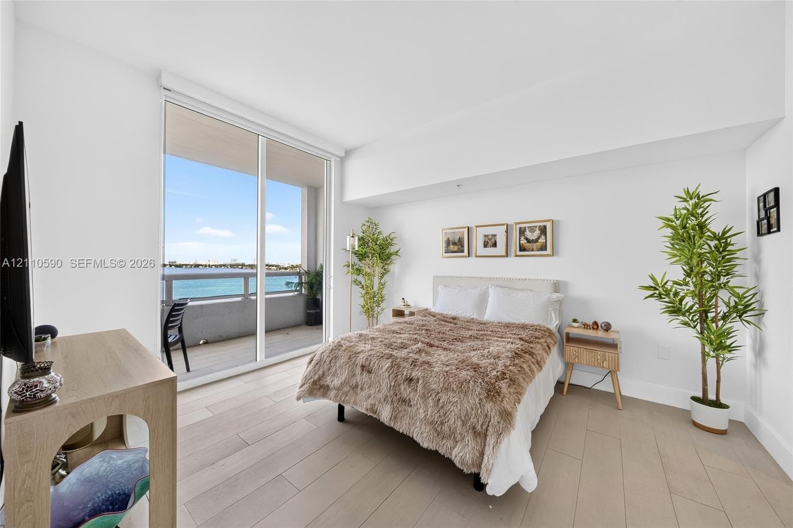 Floor-to-ceiling glass sliding doors opening to an exterior balcony with water access, wood-finish flooring, and crisp white wall finishes