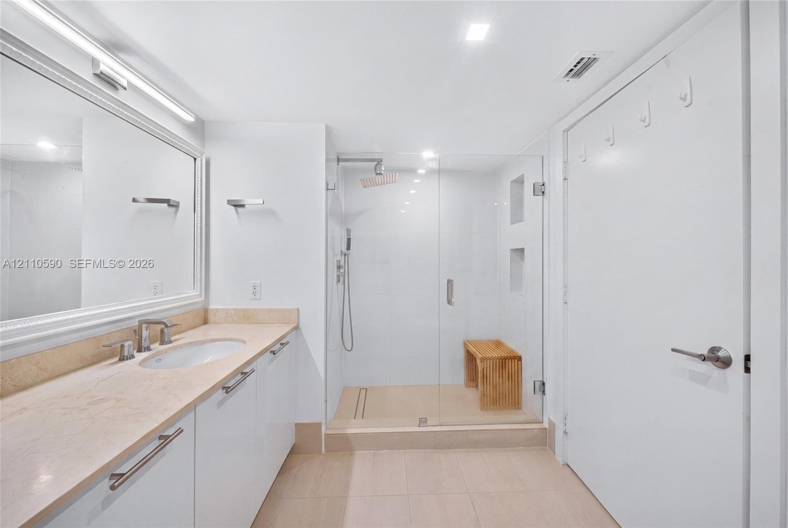 Bathroom featuring a stone-topped vanity with an integrated basin, a large wall-mounted mirror, a walk-in shower with a glass enclosure, and recessed shower wall niches