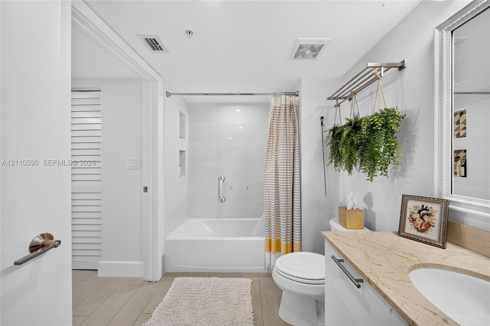 Bathroom featuring a vanity with a stone countertop, an integrated sink, white cabinetry, a soaking tub with an integrated wall niche, and wood-finish flooring