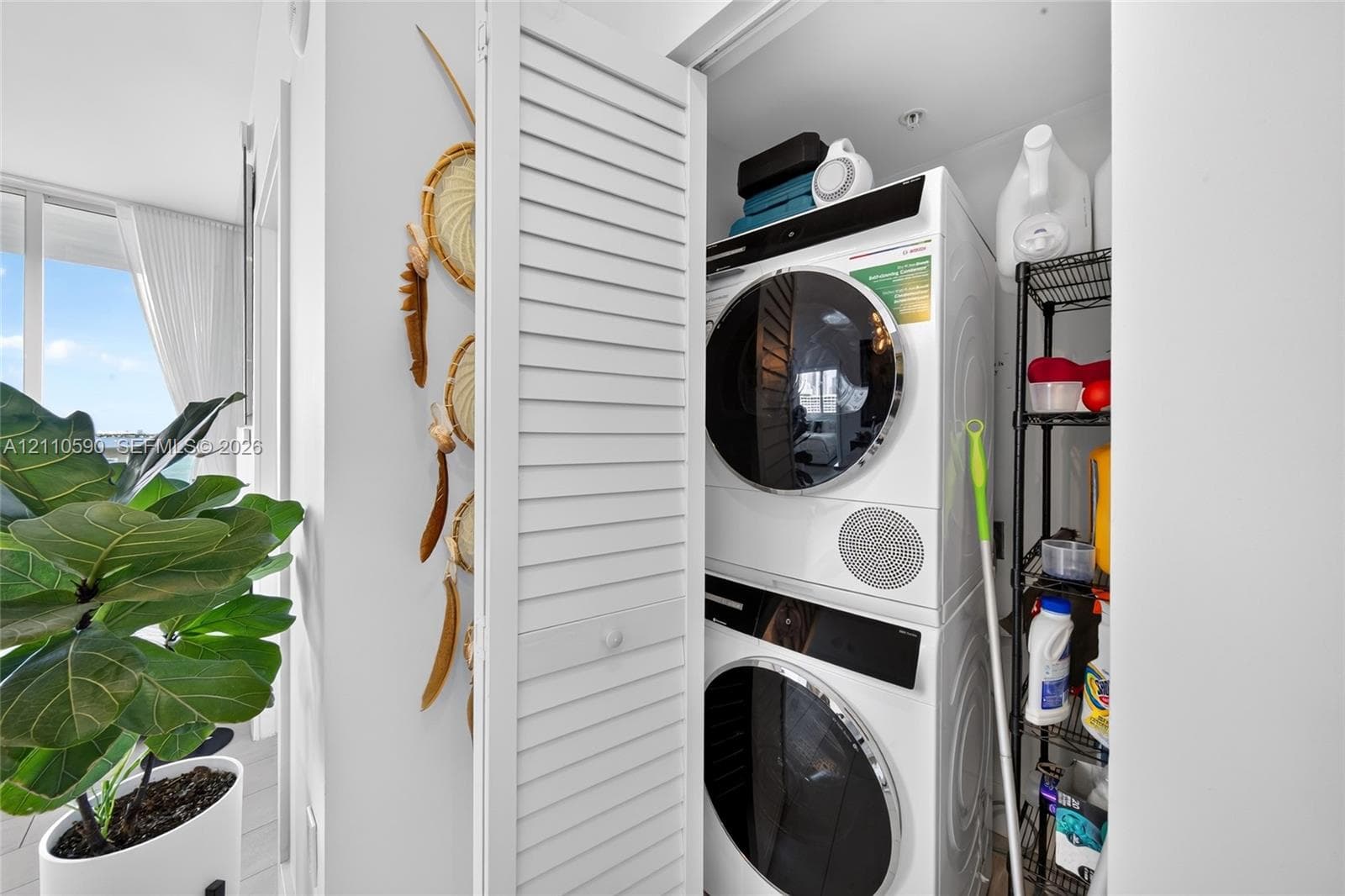 Laundry closet featuring louvered bi-fold doors and a stacked washer and dryer unit