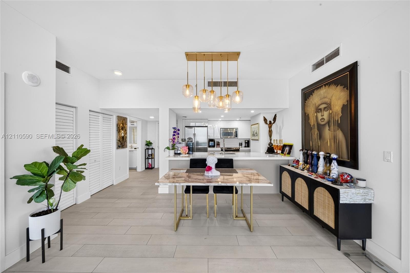 Open floor plan featuring wood-finish tile flooring, a gold multi-pendant light fixture, a quartz-topped breakfast bar, and white louvered closet doors
