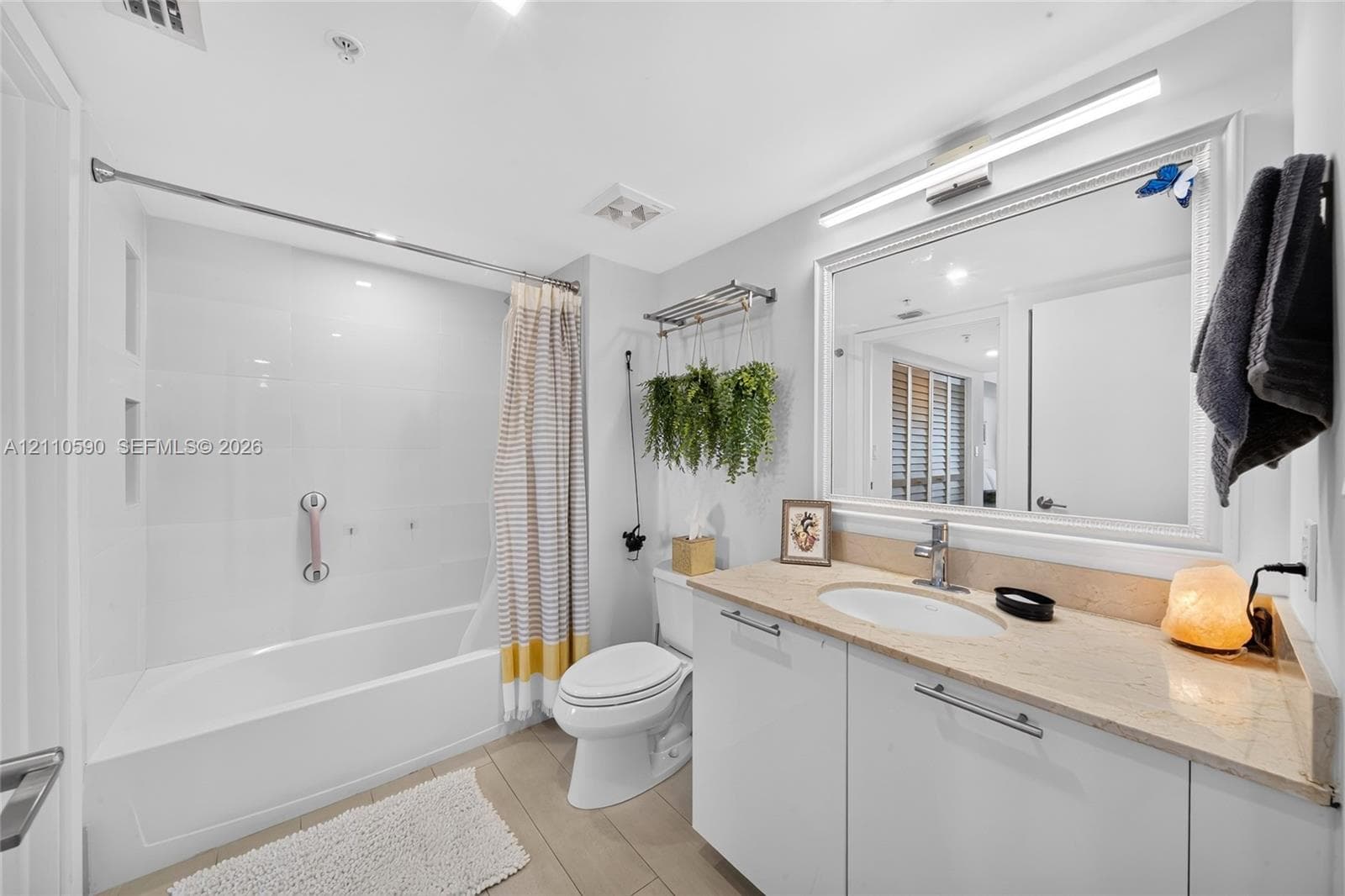 Bathroom featuring a stone-surface vanity with an integrated undermount sink, a large framed vanity mirror, built-in medicine cabinet lighting, and a tub-shower combination with a wall-mounted grab bar