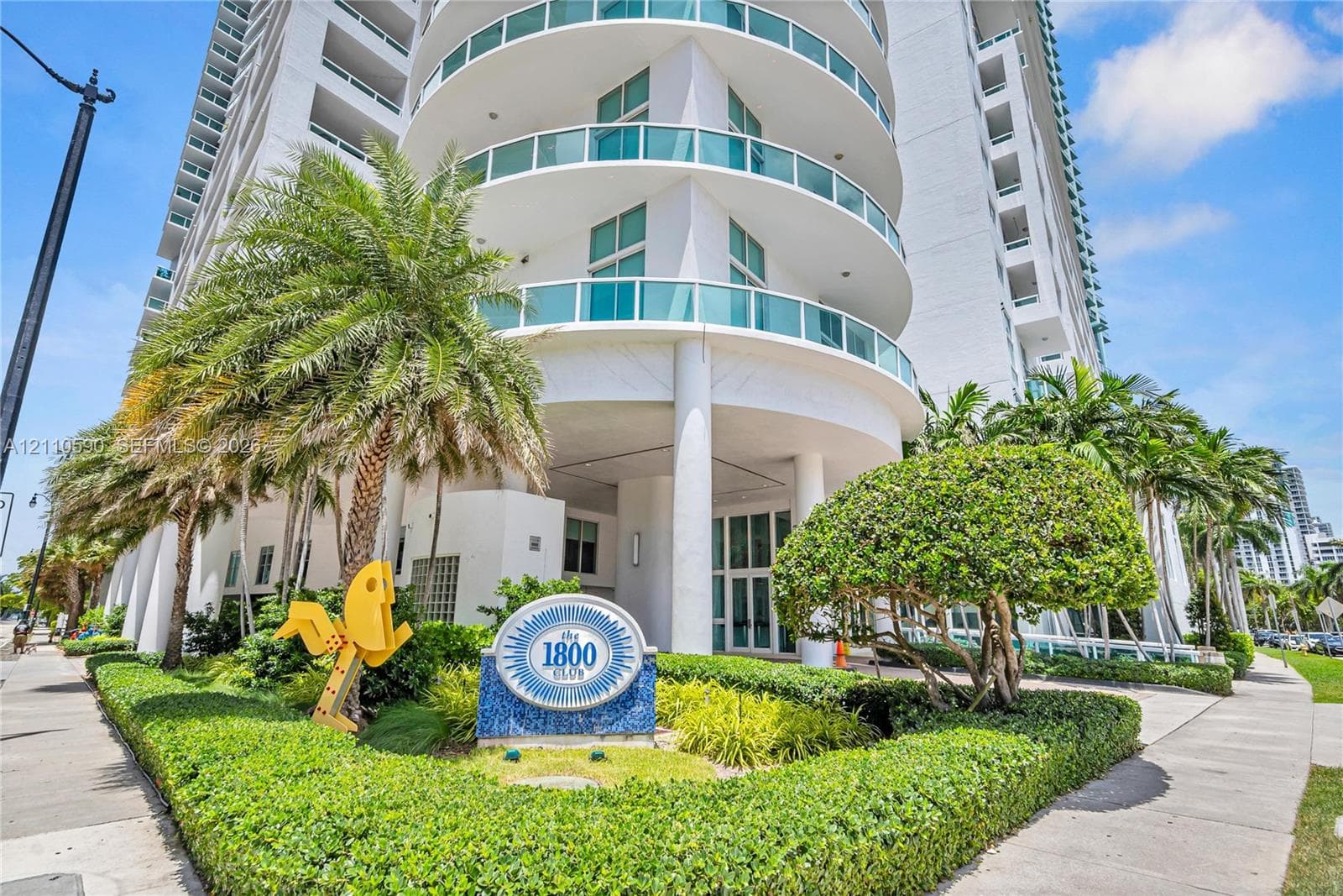High-rise exterior featuring wrap-around glass balconies, concrete architectural elements, and manicured landscaping