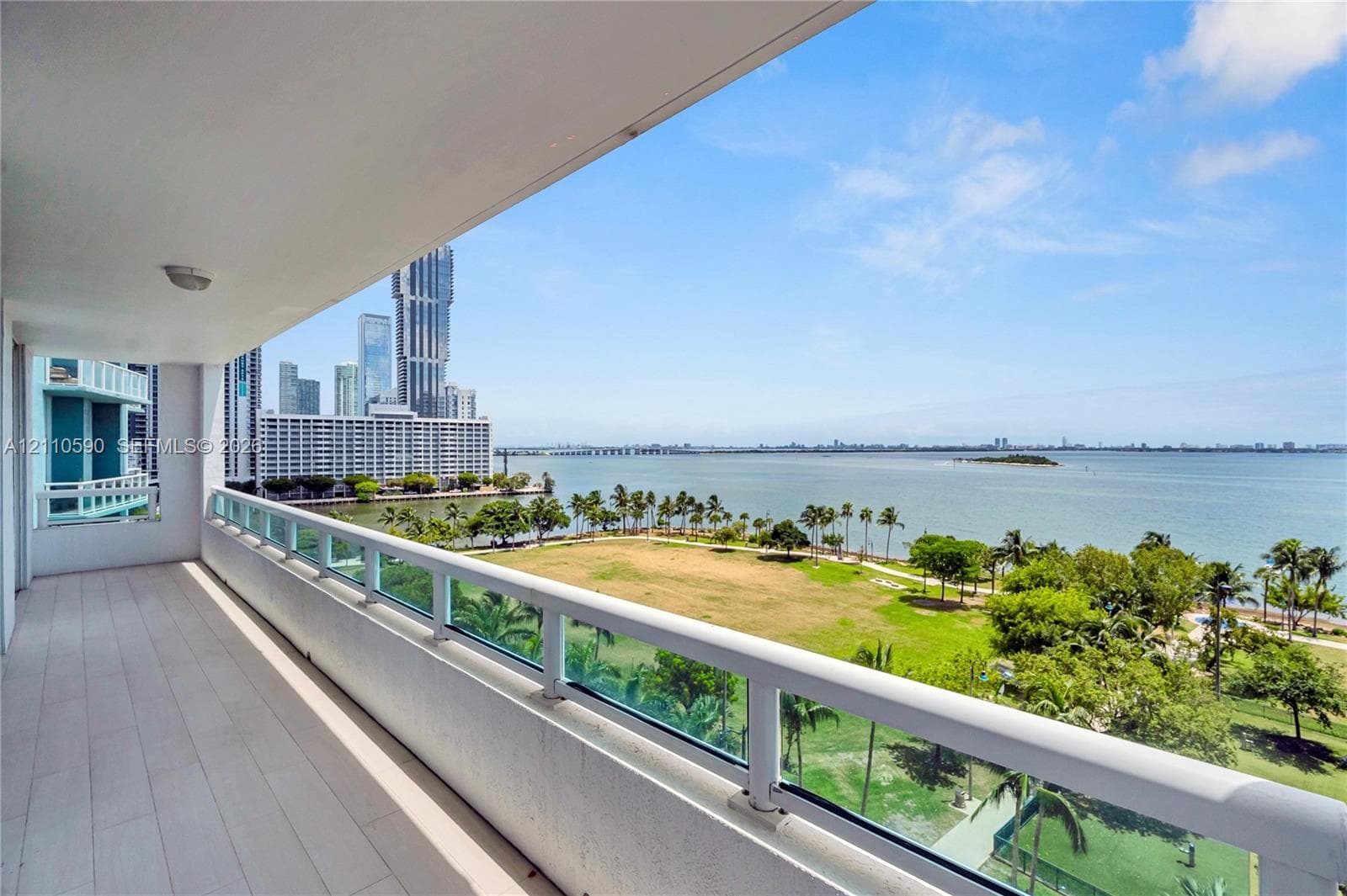 Covered balcony featuring wood-finish flooring and a glass-paneled railing overlooking the waterfront