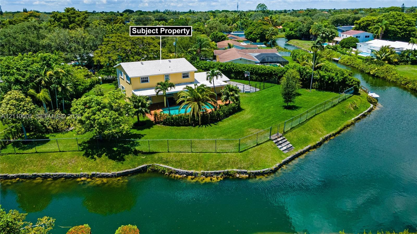 Waterfront property featuring a swimming pool, expansive lawn, stone retaining wall, and mature landscaping