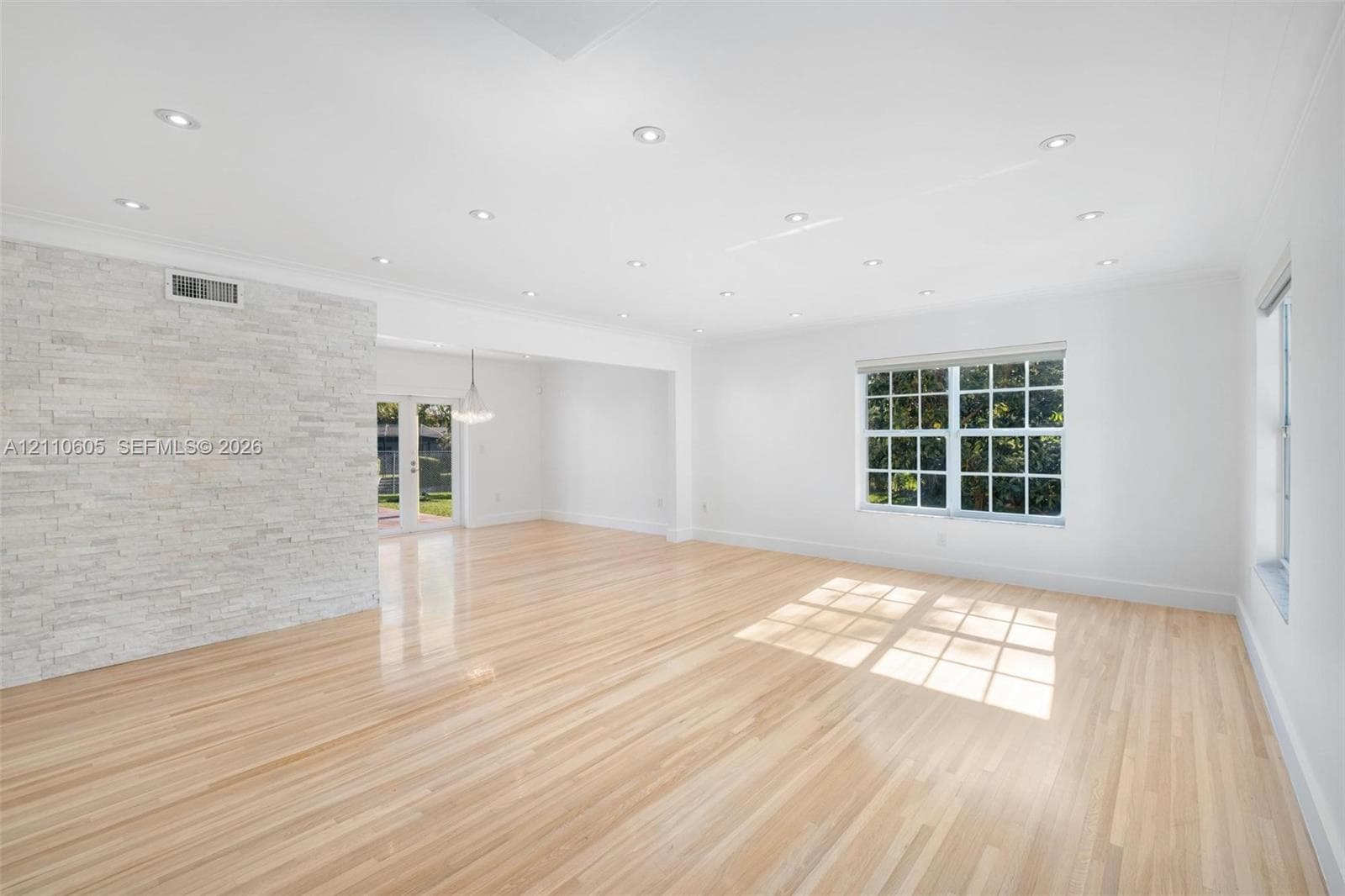 Light-toned wood flooring, textured stone accent wall, recessed ceiling lighting, and multi-pane grid windows