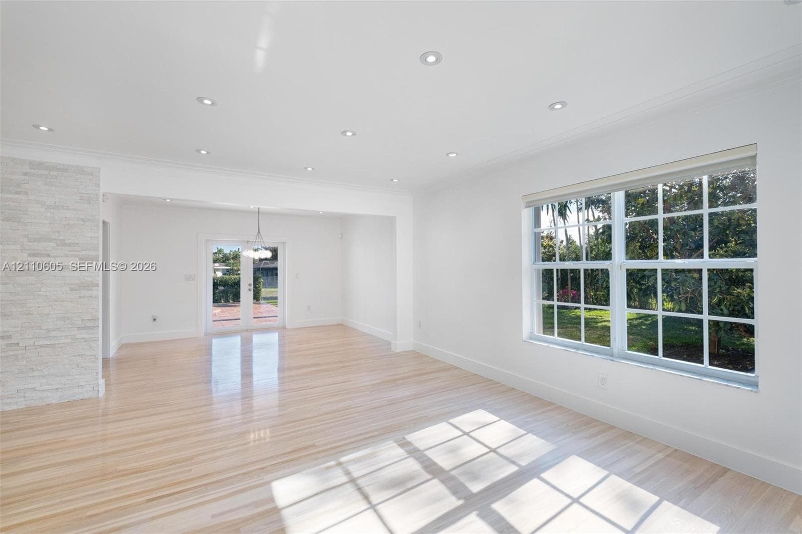 Light-filled interior featuring wood-finish flooring, recessed lighting, a stone-textured accent wall, multi-pane windows, and glass-paned double doors