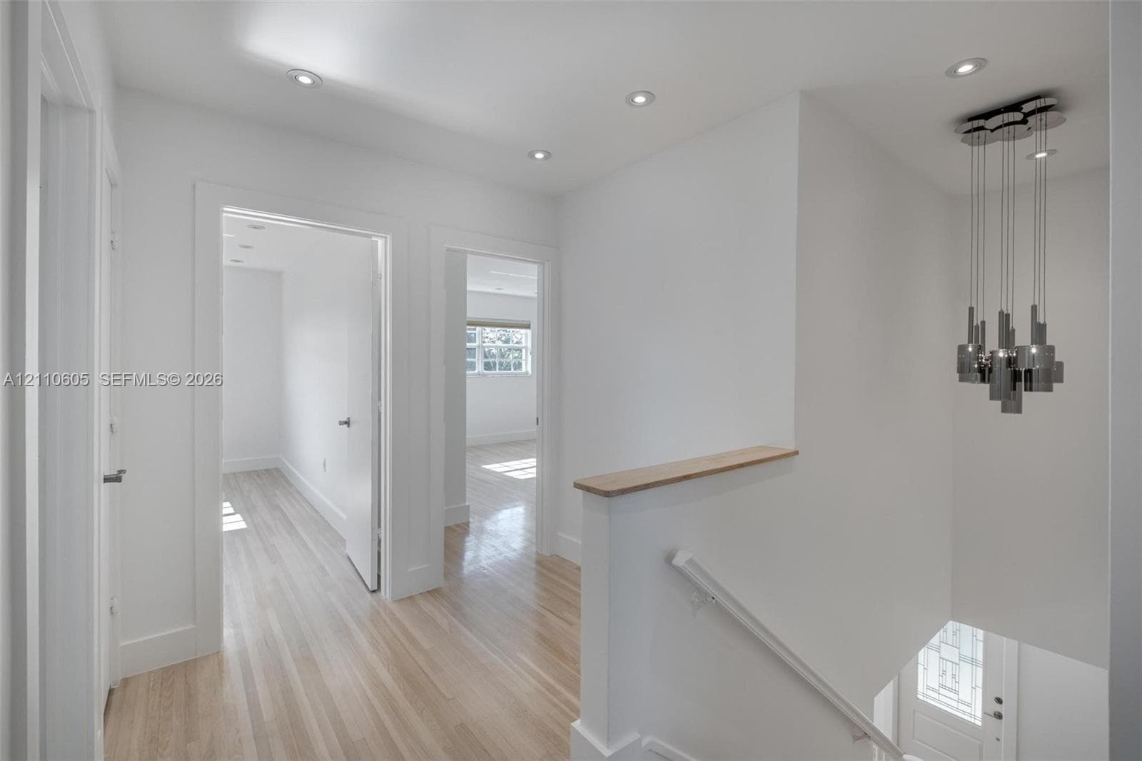 Hallway featuring wood-finish flooring, recessed lighting, a modern multi-pendant light fixture, and a staircase with a wooden handrail
