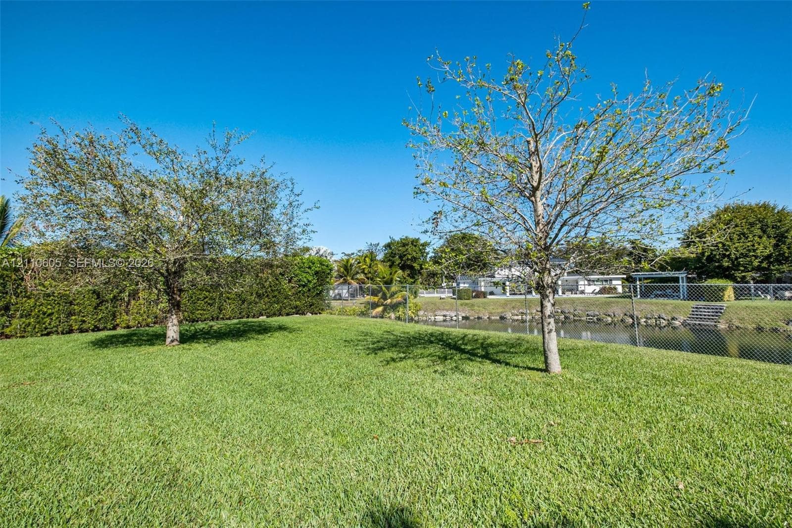Expansive lawn featuring mature trees, chain-link fencing, and water frontage