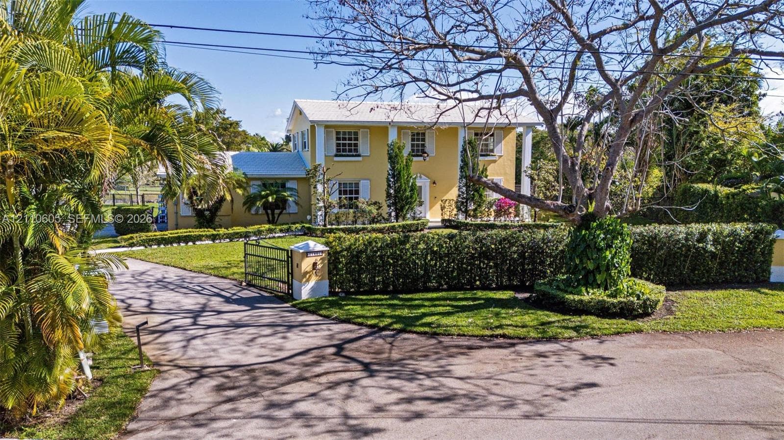Two-story exterior featuring a columned facade, multi-pane windows with shutters, metal roof, paved driveway, and established landscape