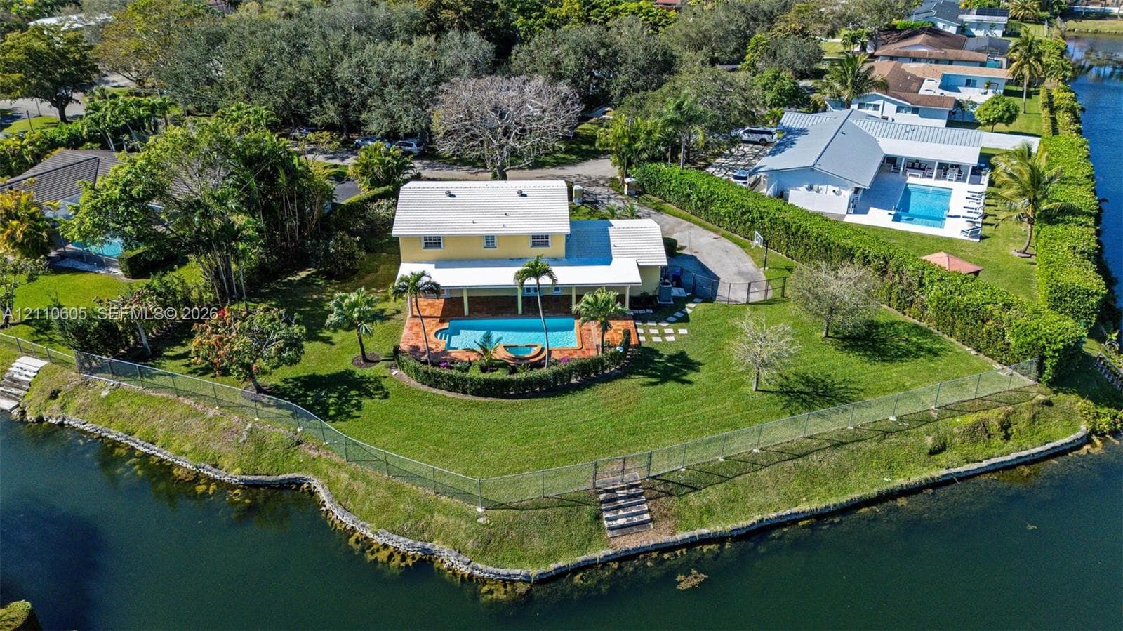 Waterfront property featuring a swimming pool, covered patio, fenced perimeter, and mature landscaping
