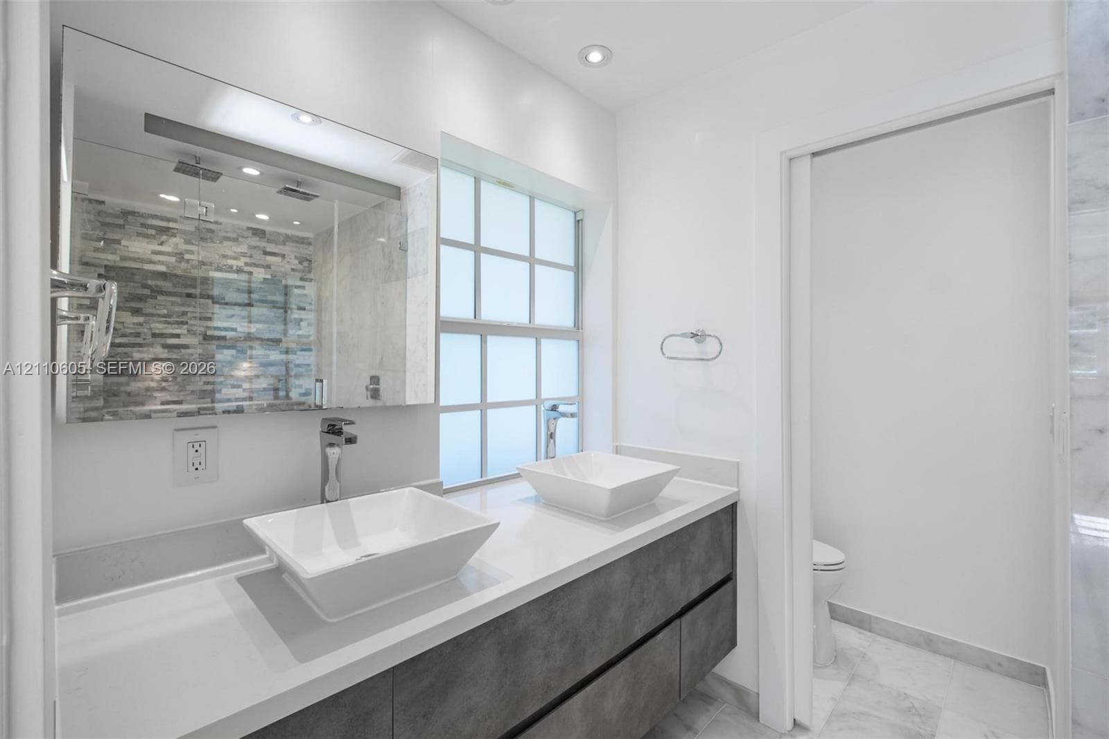 Floating dual-sink vanity with matte-finish cabinetry, white solid-surface countertops, rectangular vessel sinks, and a large frameless mirror