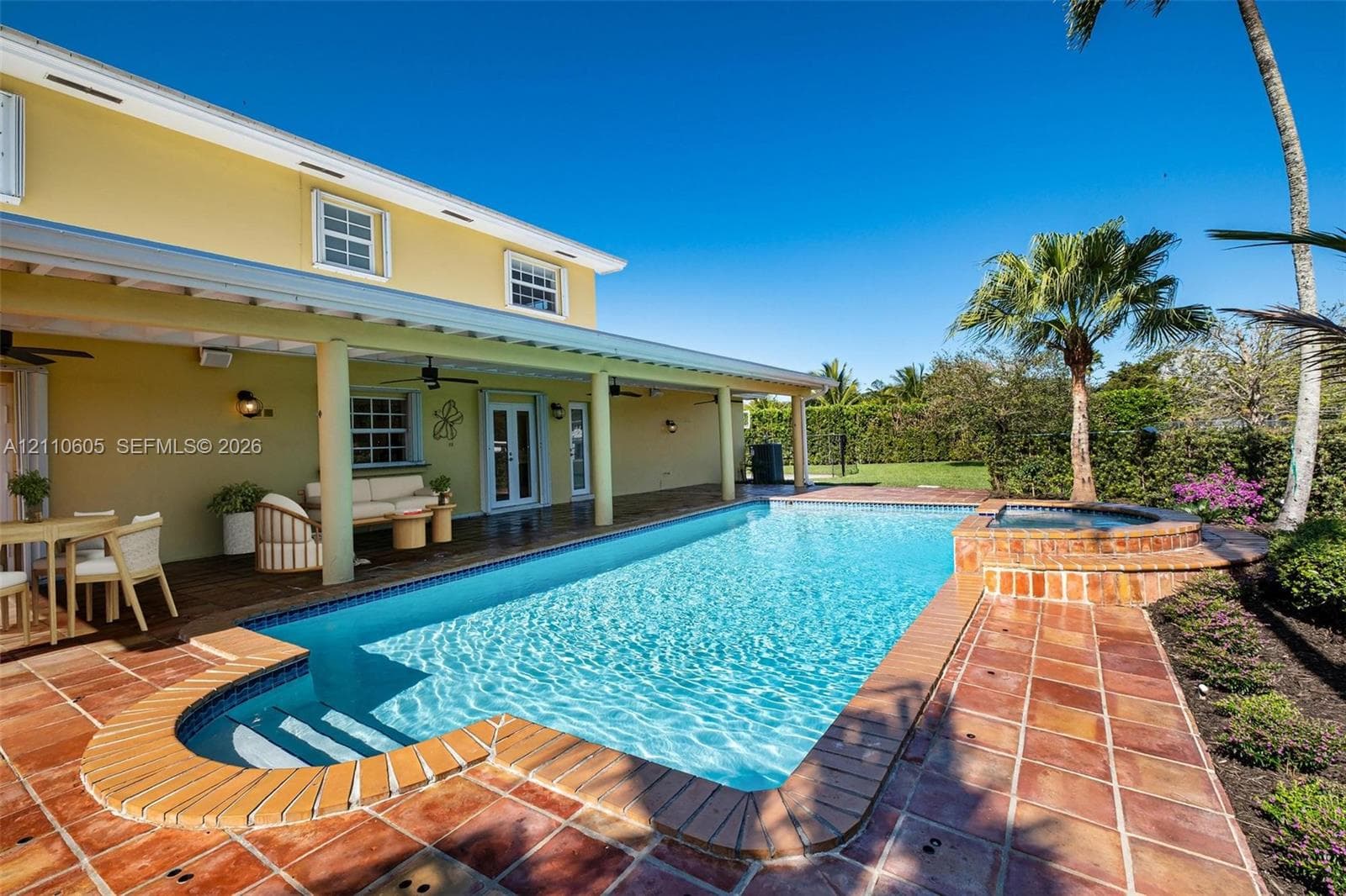 Covered patio with recessed lighting and ceiling fans, red tile pool deck, in-ground pool with integrated steps, and raised spa with brick surround