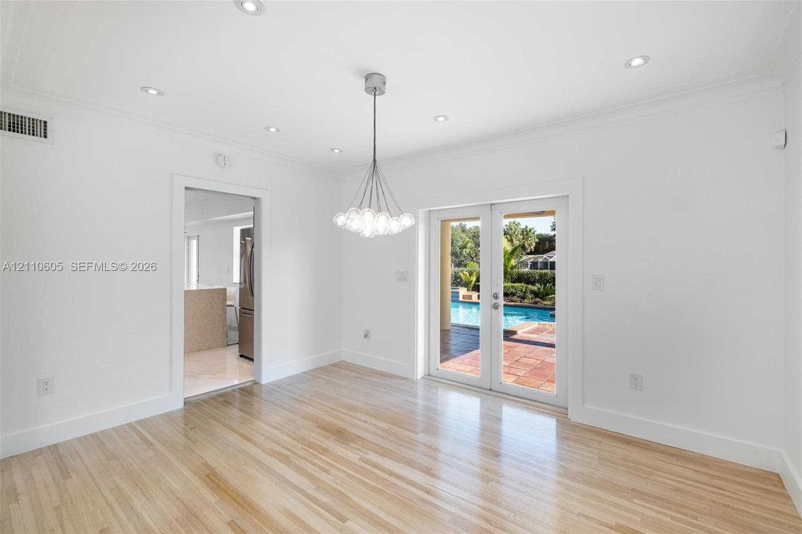 Light-filled room featuring wood-finish flooring, recessed lighting, a modern multi-light chandelier, and glass-paned double doors with access to an exterior patio and pool area