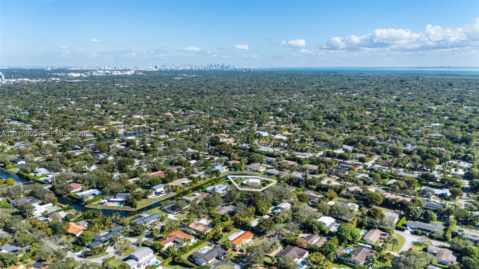 Aerial perspective of a residential lot featuring mature tree canopy, canal frontage, and suburban greenery