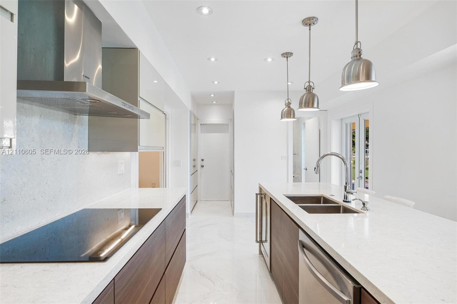 Modern kitchen featuring wood-finish flat-panel cabinetry, light-toned stone-look countertops, stainless steel appliances, marble-patterned flooring, and three pendant lights