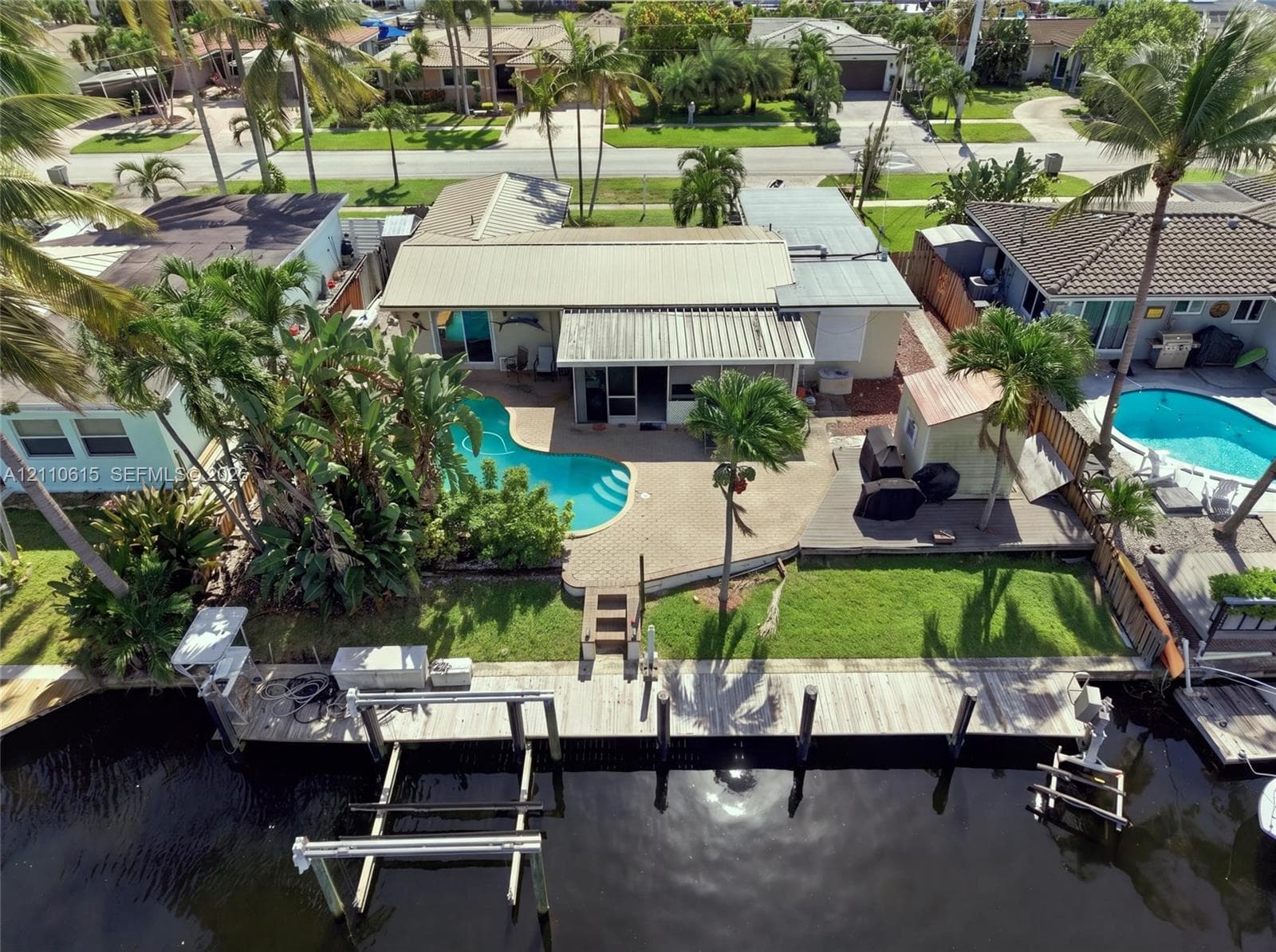 Waterfront property featuring a private boat dock, freeform swimming pool, paved patio, and mature palm landscaping