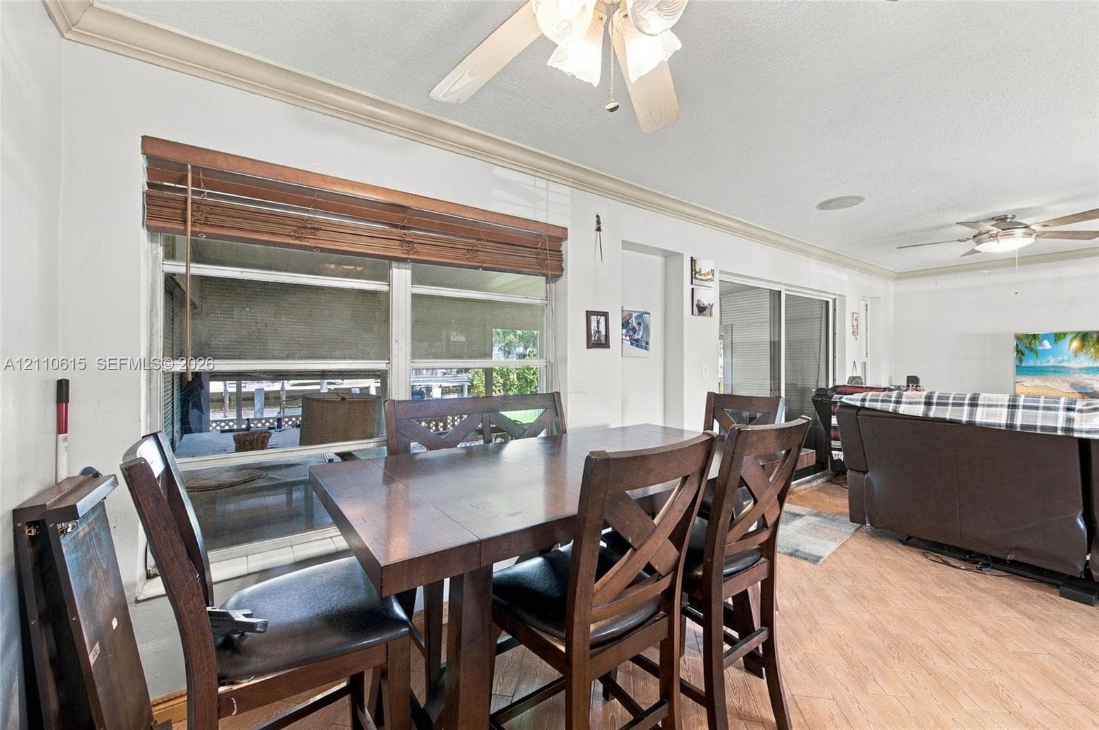 Living area featuring wood-finish flooring, two ceiling fans with integrated lighting, a triple-window configuration with horizontal blinds, and glass sliding doors