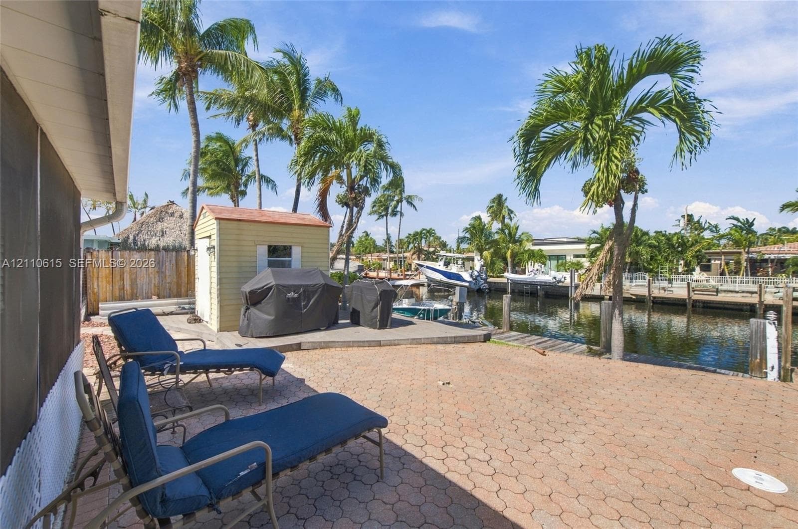 Waterfront patio featuring interlocking paver hardscaping, private dock, and mature palm trees