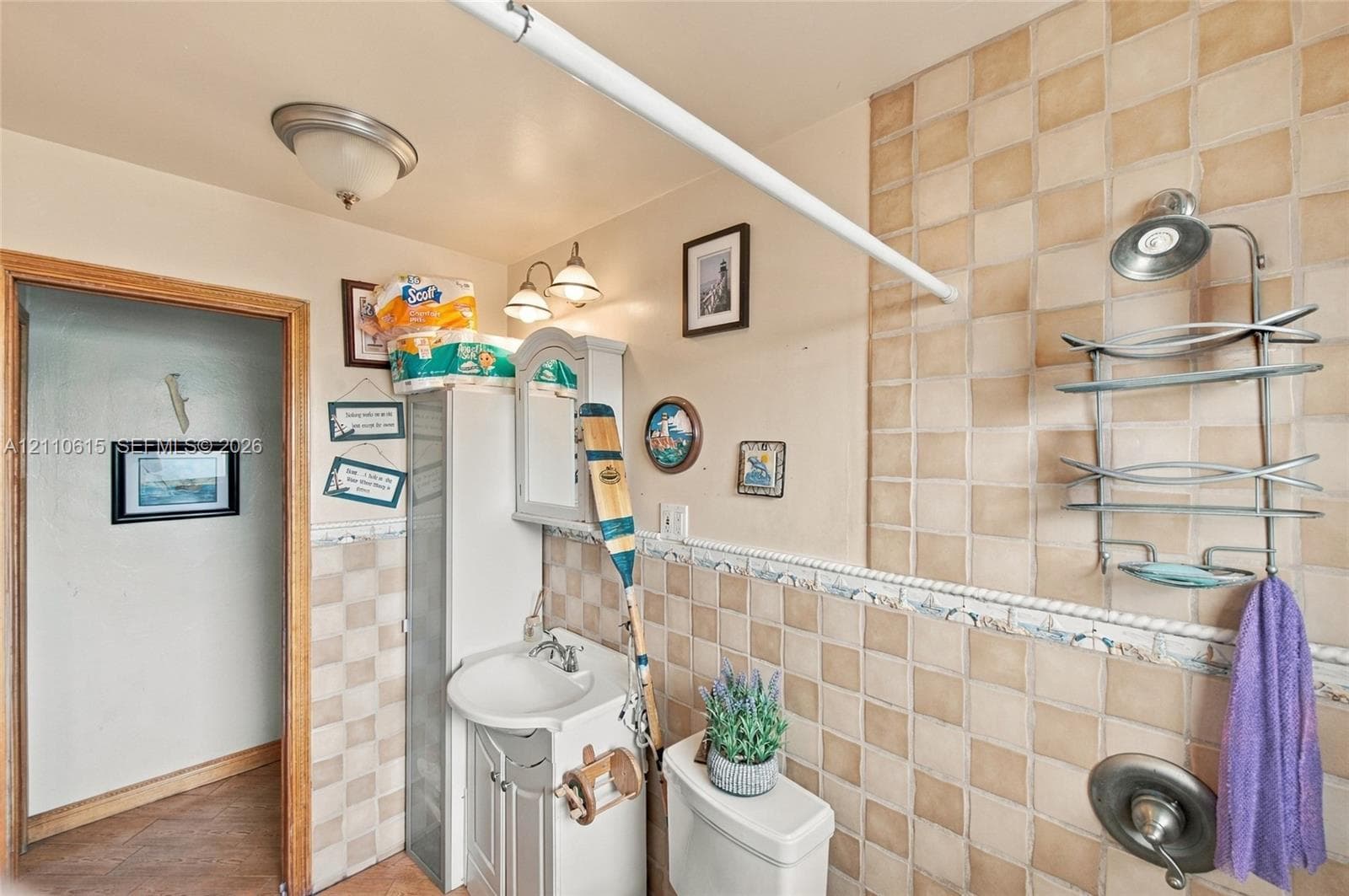 Bathroom featuring square ceramic wall tiling with a decorative border, pedestal vanity with a sink, built-in storage cabinet, and a single-handle shower valve