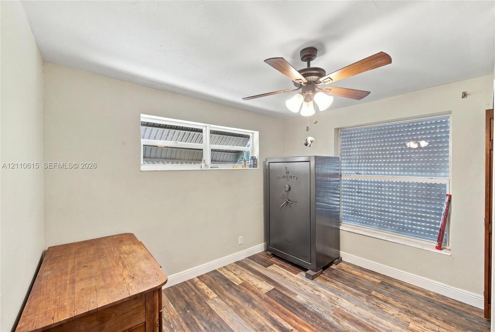 Wood-finish flooring, dual windows with exterior security shutters, and a ceiling fan with integrated lighting