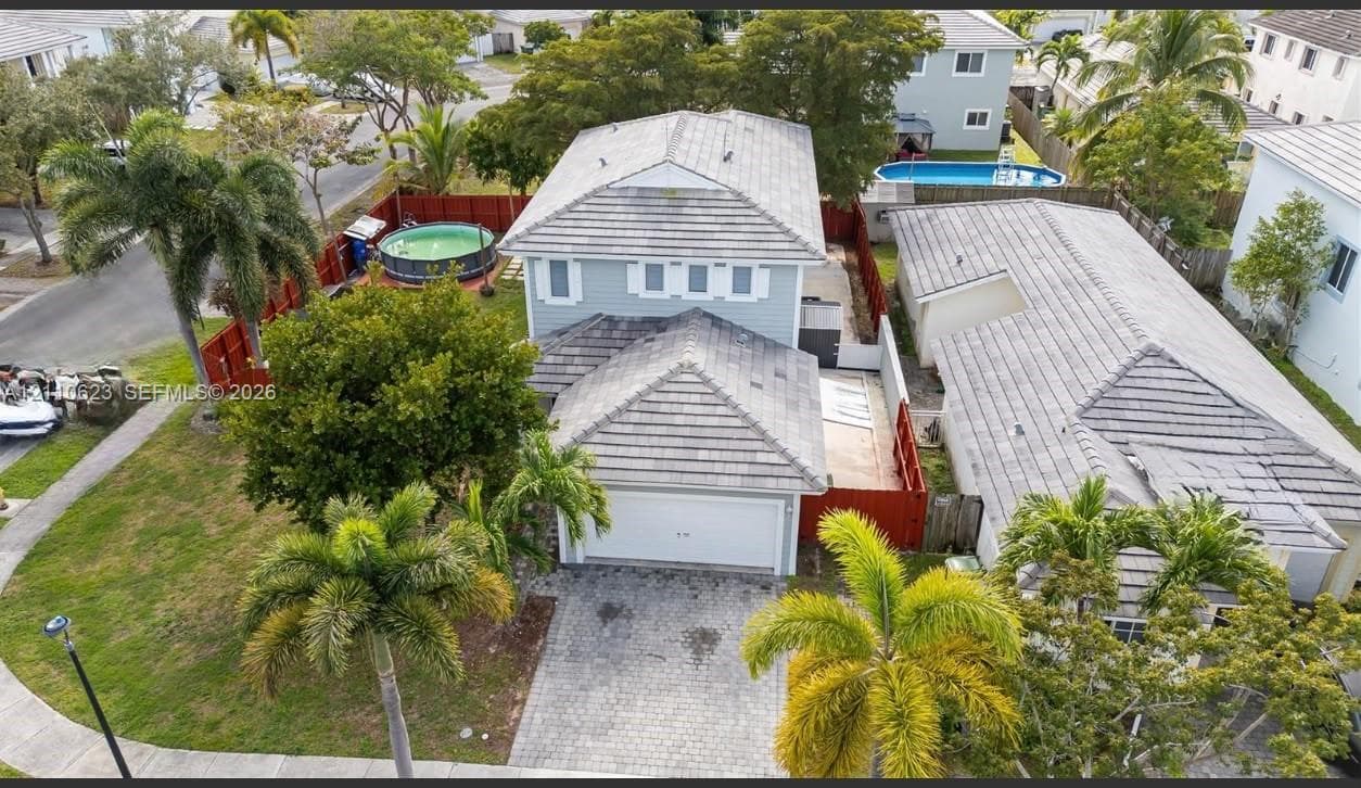 Two-story residence featuring a tile roof, paved driveway, two-car garage, and established landscaping