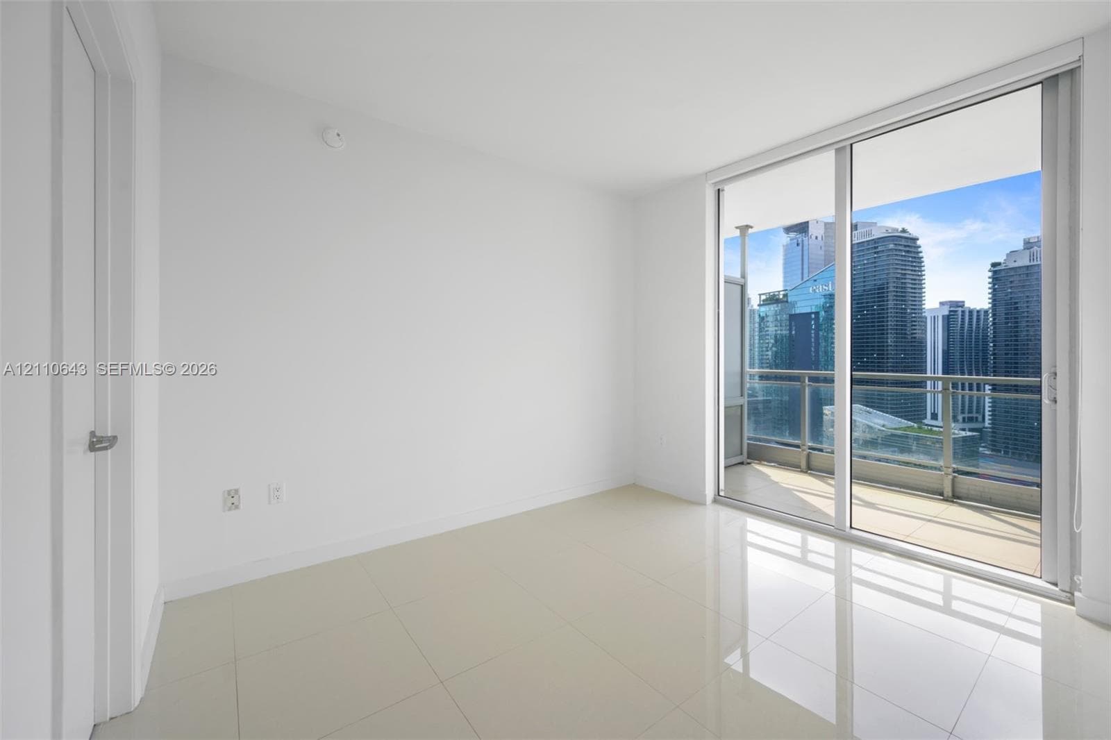 Large-format tile flooring, floor-to-ceiling glass sliding door, and private balcony with metal railing