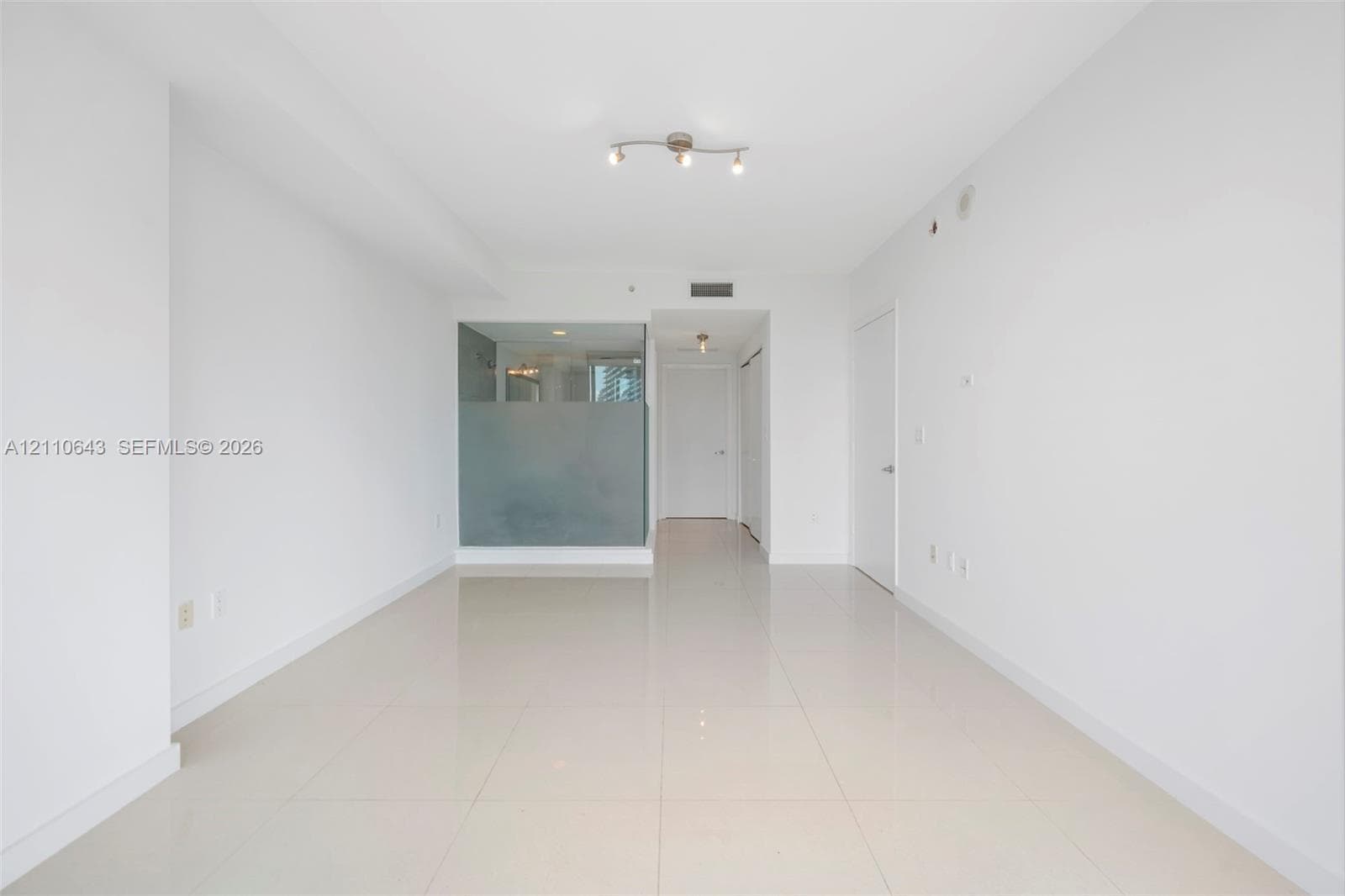 Open-concept interior featuring large-format ceramic tile flooring, neutral wall finishes, semi-opaque glass partition, and adjustable track lighting