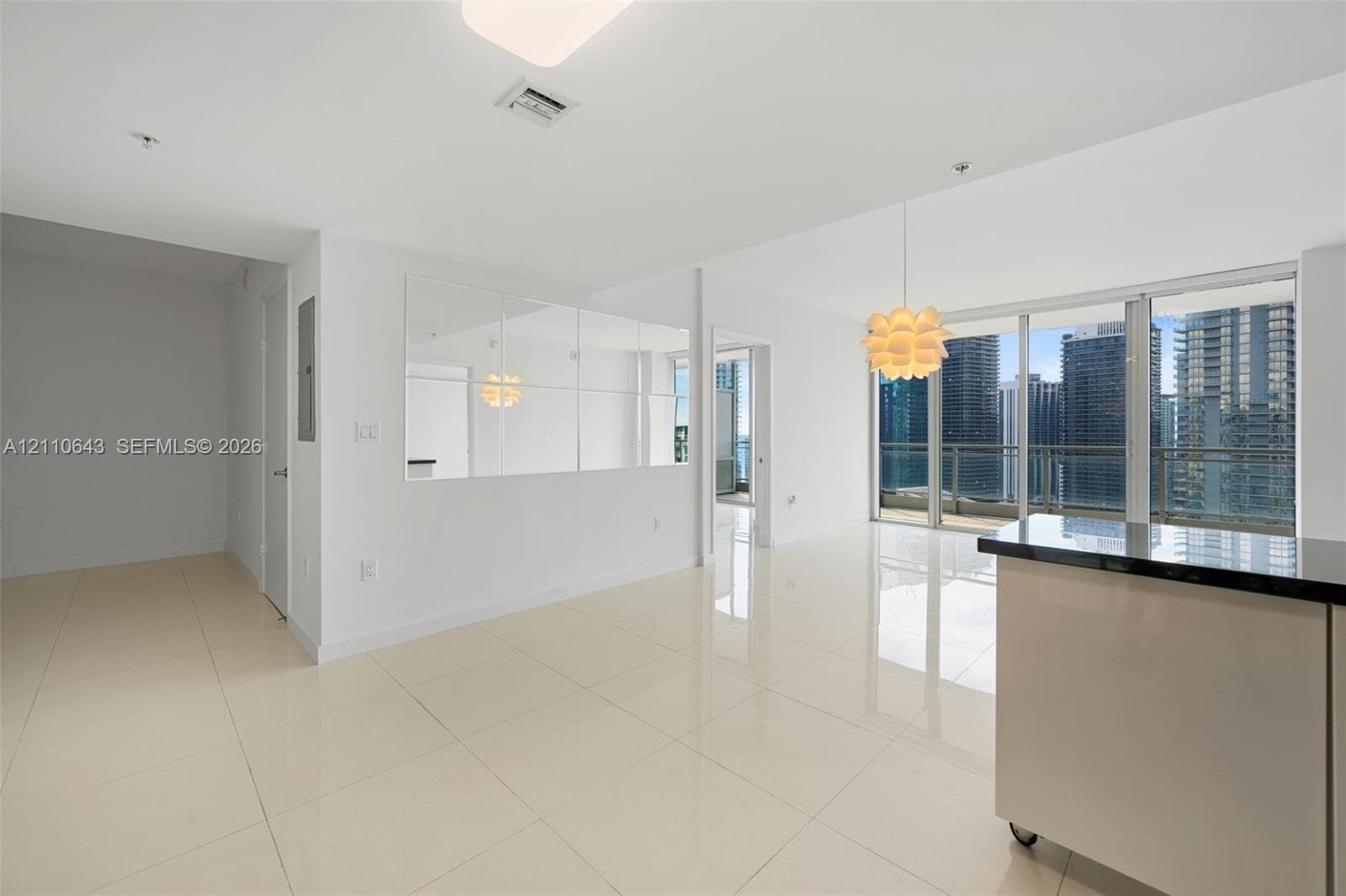 Open-concept interior featuring large-format tile flooring, floor-to-ceiling glass windows, a decorative wall-mounted mirror panel, and an island with a stone-finish countertop